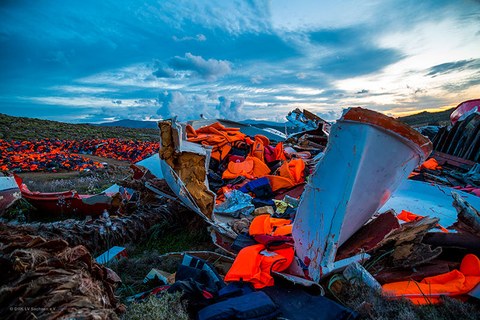 Das Foto zeigt mehrere kaputte Boote voller Rettungswesten auf einem Feld.