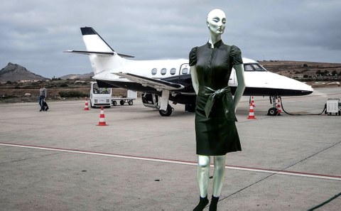 Photo: A mannequin in a black dress is standing on an airfield. In the background is a private jet.