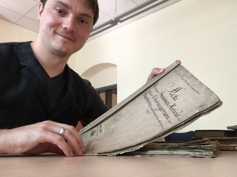 Lars Thiele lifts a document from a stack on the table and shows it to the camera.