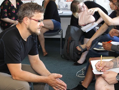 Das Foto zeigt Michael Schiefer in einem Stuhlkreis. Um ihn herum erkennt man weitere Personen.