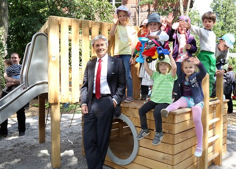 The photo shows Prof. Hans Müller-Steinhagen standing next to children sitting and standing on a piece of playground equipment. Everyone is looking at the camera. 