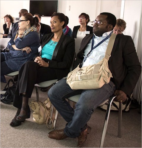 Das Foto zeigt mehrere Personen auf einer Tagung. Sie sitzen auf Stühlen und hören einem Vortrag zu.