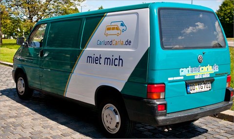 The photo shows a geen Volkswagen EuroVan. The side of the van shows the "Carl und Carla" logo and a slogan saying "rent me".