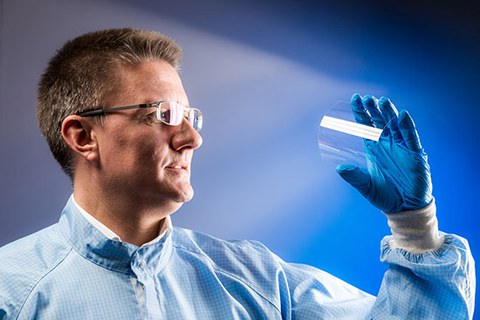 Das Foto zeigt Uwe Beier. Mit einer Hand biegt er ultradünnes Glas und betrachtet es dabei.