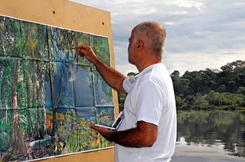 Das Foto zeigt Yadegar Asisi. Er steht vor einer Leinwand und malt.