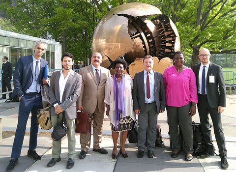Seven people stand in a line in front of the Sphere Within a Sphere statue, a large, bronze globe with a chunk missing, revealing the inside.