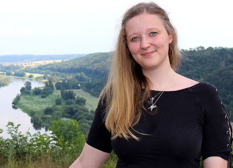 Photo portrait of Stefanie Gentzsch. Behind her we see a river and a tree-covered hill.