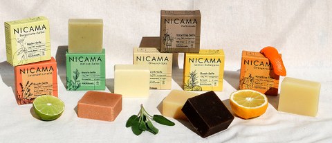 A product display featuring bars of soap and solid shampoo plus natural ingredients such as a lime, an orange and sage.