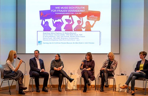 Picture of 5 women and 1 man engaged in discussion on a stage in front of a projected image on a screen. Christiane Bonk is on the center right.