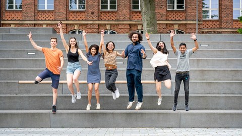 Gruppe von Studierender spring auf einer großen Treppe in die Luft