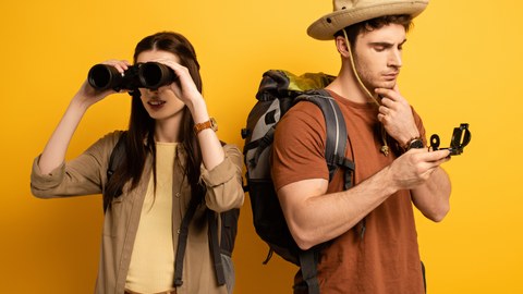The picture shows a young woman and a young man. She is looking through binoculars, he is looking at a compass.