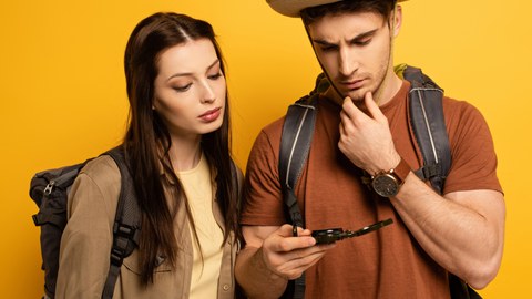The picture shows a young woman and a young man. They both look skeptically at a compass.