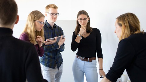 5 Stipendiat/innen stehen im Kreis und beraten über einem Flipchart