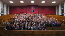 200 Studierende im Hörsaal frontal mit erhobenen Armen