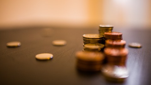 Das Foto zeigt mehrere Stapel an Münzgeld auf einem Tisch. Weiterhin liegen vereinzelte Geldstücke auf dem Tisch.