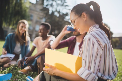 Internationale Studierende sitzen auf einer Wiese im Sonnenschein und sind fröhlich