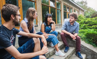 Im Freien sitzen vier ERASMUS Studenten auf einer Treppe und unterhalten sich.