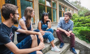 Im Freien sitzen vier ERASMUS Studenten auf einer Treppe und unterhalten sich.
