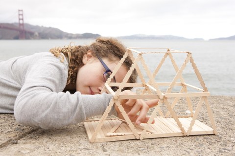 Foto von Mädchen, dass vor Meereskulisse an einem Holzmodell baut