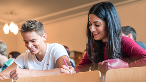 zwei Studierende sitzen in einem Hörsaal und schreiben