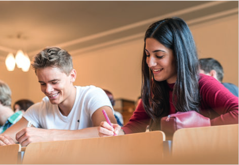 zwei Studierende sitzen in einem Hörsaal und schreiben