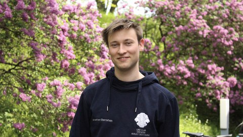 Portrait von Jonathan Sternstein vor blühenden Büschen