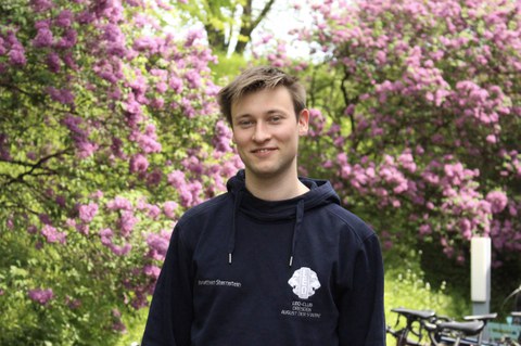 Portrait von Jonathan Sternstein vor blühenden Büschen