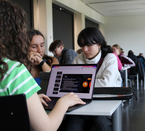 Drei Jugendliche sitzen um einen Laptop auf dem eine Präsentation zum Thema Astrophysik zu sehen ist.