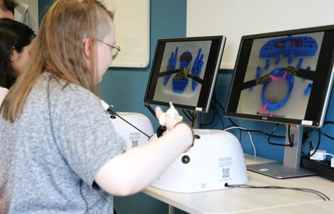 Das Foto zeigt eine Schülerin, die an einem Simulator sitzt, welches mit einem Bildschirm verbunden ist.