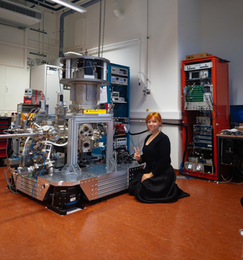 Das Bild zeigt eine junge Frau, die vor einer großen Appartur kniet, die in einem Labor steht.