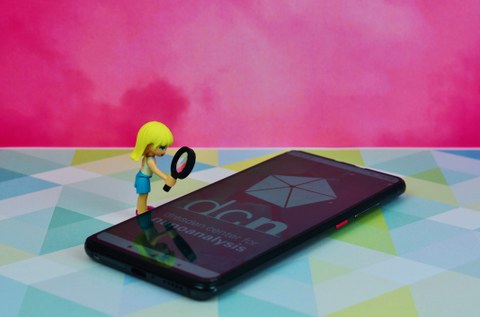Das Bild zeigt ein weiblich Legofigur die mit einer Lupe auf ein Handy schaut.