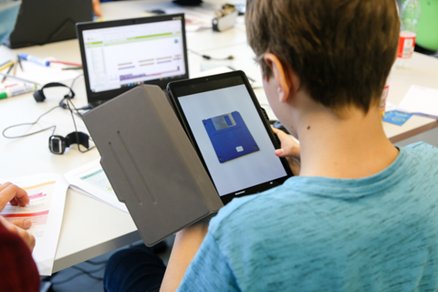 Das Foto zeigt einen Schüler von hinten der ein Tablet hält.