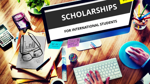 Bild eines Arbeitsplatzes mit Computer. Auf dem Desktop stehen groß die Worte "SCHOLARSHIPS FOR INTERNATIONAL STUDENTS".