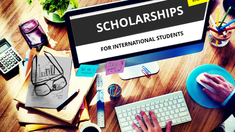 Picture of a workstation with a computer. On the desktop, the words "SCHOLARSHIPS FOR INTERNATIONAL STUDENTS".