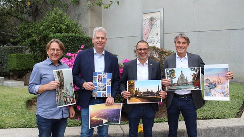 Die 3 Schulleiter des Colegio Aleman Humboldt in Mexiko Stadt und der Studienberater stehen vor der Schule und halten Bilder von Dresden in die Kamera