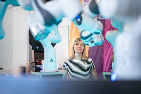 Zwischen Roboterarmen steht ein Mädchen im schwarz-weiß gestreiften T-Shirt und betrachtet diese.