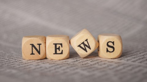 Foto mit vier Holzwürfeln, die auf einem bedruckten Blatt Papier liegen. Auf jedem Würfel steht ein Buchstabe. Die Buchstaben ergeben das Wort "News".