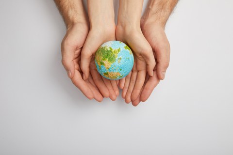 Kinderhände halten, unterstützt von erwachsenen Händen, einen Globus