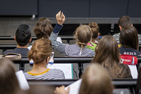 Studierende in einer Vorlesung im Hörsaal, eine Studierende meldet sich