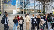 Jugendliche stehen in Halbkreis vor Glasfassade des Hörsaalzentrums und hören Vortrag