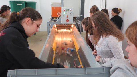 Foto einer Sortiermaschine für Plastikmüll. Das Laufband wird von Schülerinnen mit Plastikmüll befüllt. Die anderen schauen interessiert zu.