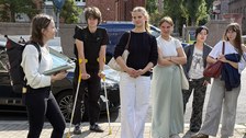 Jugendliche unterhalten sich. Sie stehen an draußen auf einem Pfalsterweg, mit Backsteingebäuden im Hintergrund. 