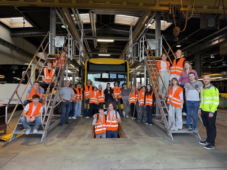 Eine Gruppe junger Menschen in Warnwesten steht um einen Elektrobus in Gelb. Seitlich stehen die Personen auf Treppen.