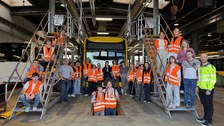 Eine Gruppe junger Menschen in Warnwesten steht um einen Elektrobus in Gelb. Seitlich stehen die Personen auf Treppen.