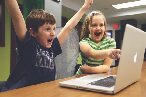 Zwei Kinder freuen sich und schauen auf einen Laptop