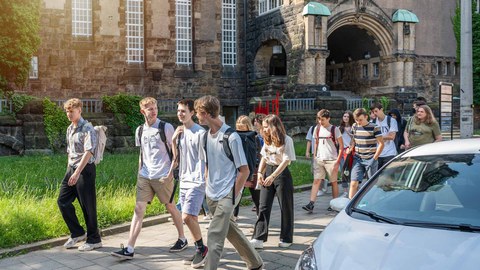 Foto einer Gruppe von jungen Leuten, die hintereinander auf einem Bürgersteig laufen. 