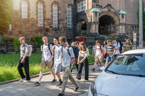 Foto einer Gruppe von jungen Leuten, die hintereinander auf einem Bürgersteig laufen. 