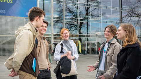 Drei Schüler und zwei Schülerinnen unterhalten sich vor der Glasfront eines Gebäudes