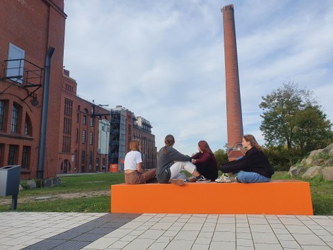Vier Mädchen sitzen vor einem Industriegebäude aus Backstein.