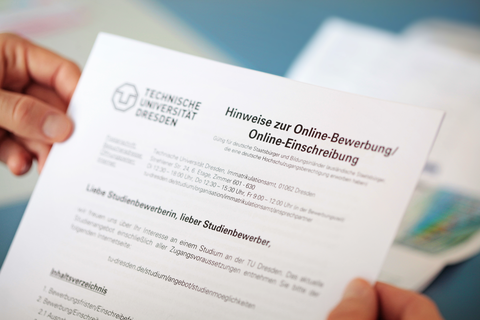 Das Foto zeigt die Hände einer Person. In diesen hält sie ein Formular mit der Aufschrift: "Hinweise zur Online-Bewerbung/Online-Einschreibung"